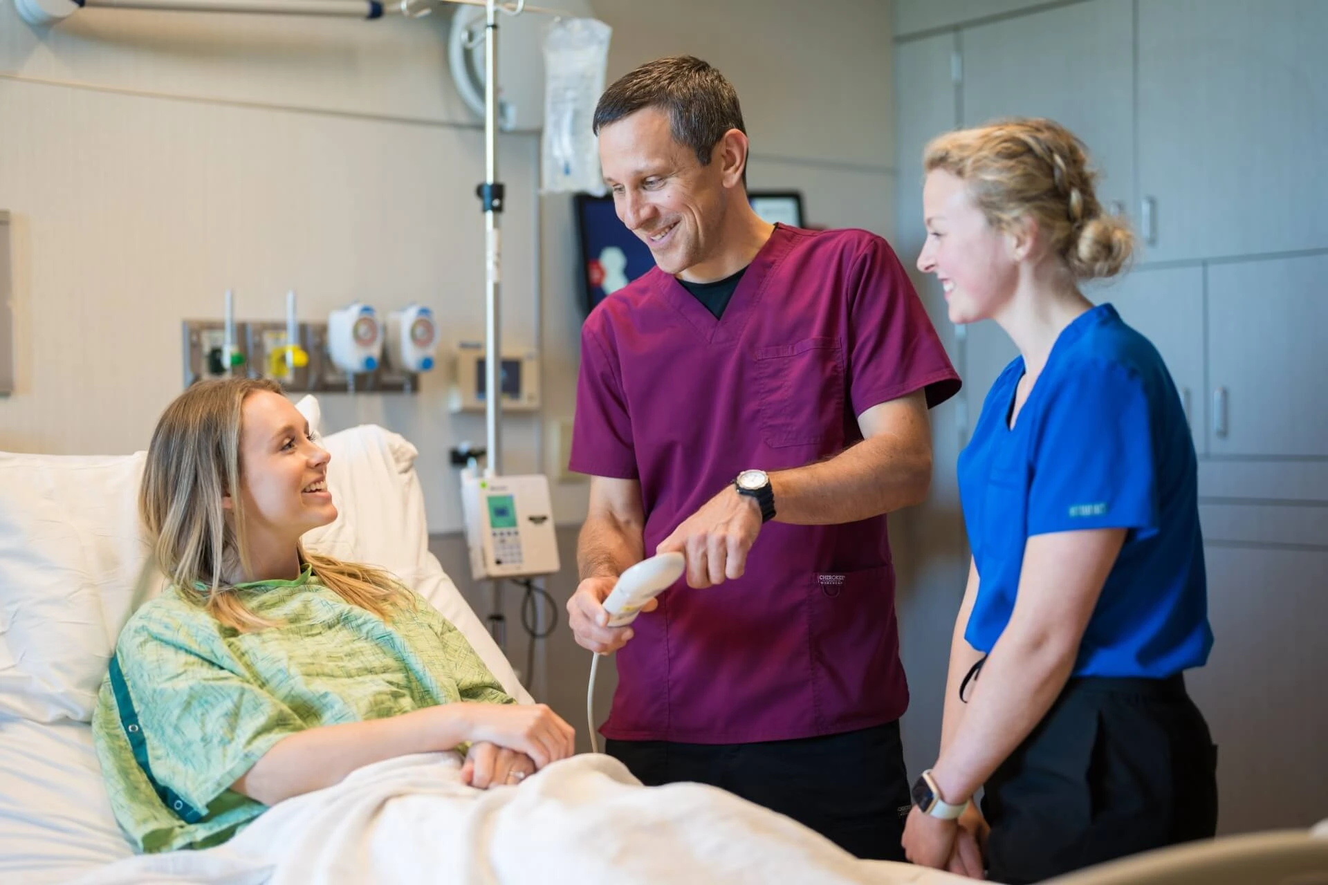 Two healthcare workers speak with a patient lying in a hospital bed 